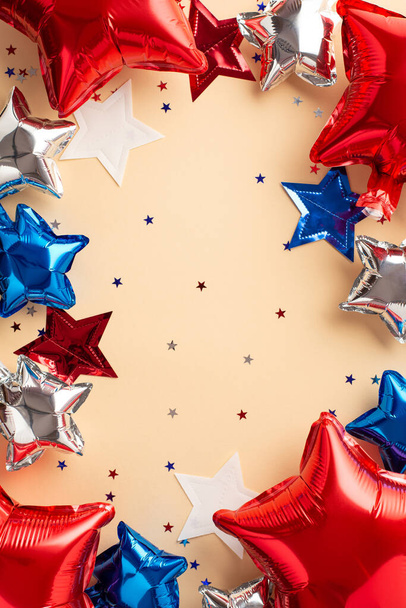 USA Independence Day concept. Top view vertical photo of balloons in national flag colors star garland and confetti on isolated beige background with blank space in the middle - Photo, Image