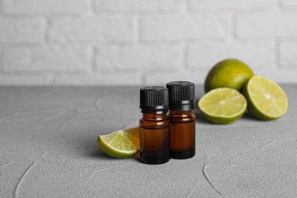 Bottles of essential oil with limes on grey table, closeup - Foto, Imagem