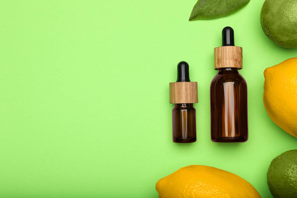 Bottles of citrus essential oil and fresh fruits on green background, flat lay. Space for text - Fotó, kép