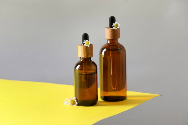 Bottles of chamomile essential oil and flowers on color background - Photo, Image