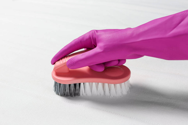 Woman in purple gloves cleaning white mattress with brush, closeup - Foto, afbeelding