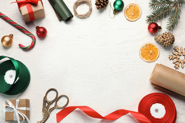 Ένα πλαίσιο από κουτιά δώρων. Χριστουγεννιάτικη διακόσμηση, ψαλίδι, κορδέλα και χαρτί περιτυλίγματος σε λευκό ξύλινο τραπέζι, επίπεδο lay. Χώρος για κείμενο - Φωτογραφία, εικόνα