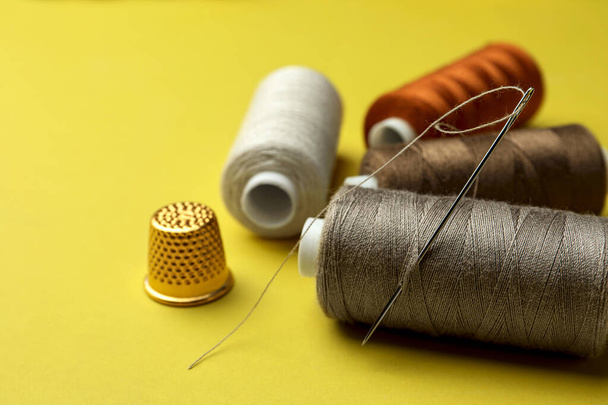 Different colorful sewing threads with needle and thimble on yellow background, closeup - Φωτογραφία, εικόνα