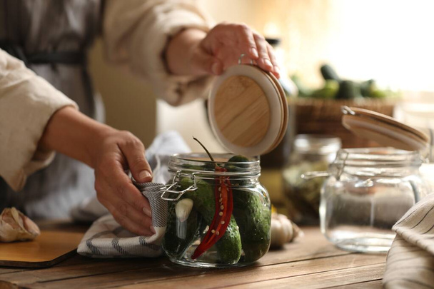 Woman pickling glass jar of cucumbers at wooden table, closeup - Foto, imagen