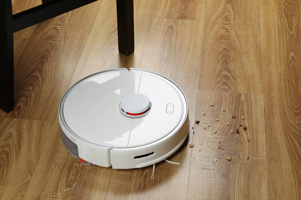 Robotic vacuum cleaner removing dirt from wooden floor indoors - Фото, изображение