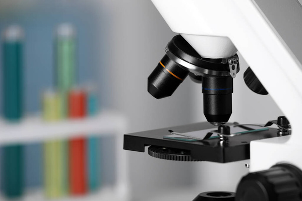 Σύγχρονο ιατρικό μικροσκόπιο με γυάλινη διαφάνεια σε θολή φόντο, κοντινό πλάνο. Χώρος για κείμενο - Φωτογραφία, εικόνα