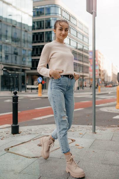 Cool girl in sweater looks away. Lifestyle portrait of a young stylish woman walking outdoors. Lifestyle portrait of a young woman in sweater standing on the street in Warsaw. - Zdjęcie, obraz