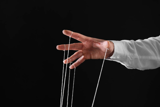 Man pulling strings of puppet on black background, closeup. Space for text - Fotoğraf, Görsel