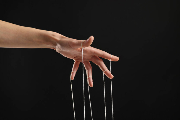 Woman pulling strings of puppet on black background, closeup - Valokuva, kuva