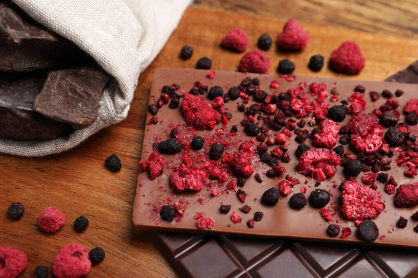 Different chocolate bars with freeze dried fruits on wooden board, closeup - 写真・画像