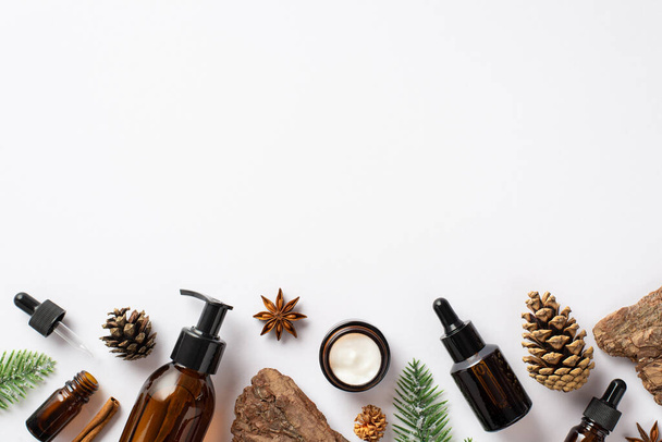 Organic skincare cosmetics concept. Top view photo of amber glass bottles fir branches pine bark cones and anise on isolated white background with copyspace - Foto, Imagem