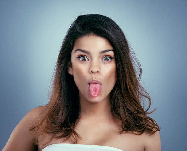 Gorgeous can be silly too. Studio shot of a beautiful young woman sticking out her tongue against a blue background - Foto, Imagen