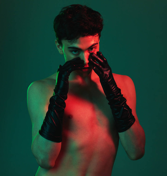 Beauty, sensual and model with a shirtless man posing in studio on a green background with light for creative art. Portrait, topless and desire with a sexy young male in gloves proud of his body. - Фото, изображение