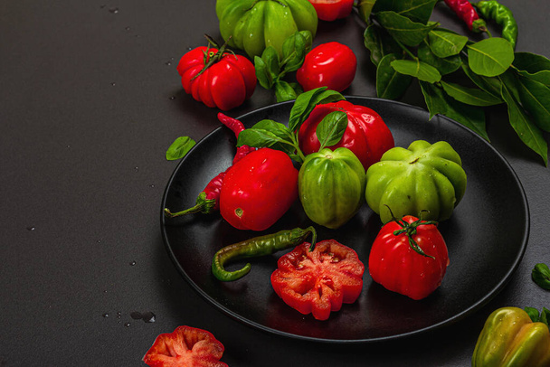 Grüne und rote gerippte Tomaten, amerikanische oder florentinische Sorte. Reifes Gemüse, Chili, frische Lorbeerblätter. Trendy hartes Licht, dunkler Schatten, Steinbetonhintergrund, flache Verlegung, Kopierraum - Foto, Bild