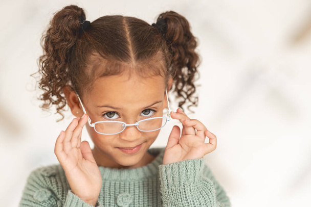 Kleines Mädchen, Brille und Sehbild mit einem Kind, das eine Brille in einem Brillengeschäft zur Augenpflege trägt. Optometrie, Augenheilkunde und niedliches weibliches Kind posieren mit Brille und Linsen im Einzelhandel. - Foto, Bild