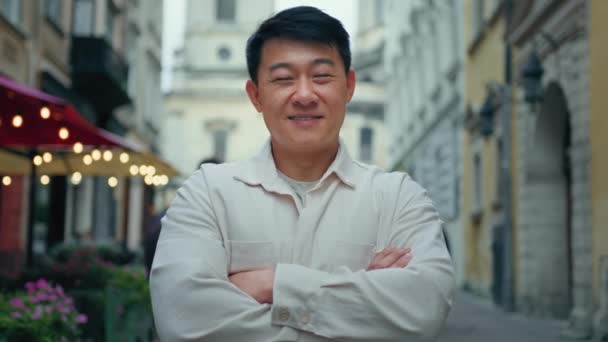 Happy potěšen sebevědomý muž stojící venku radostné mužské turistické stojí v centru města při pohledu na kameru usmívající se asijský model pózuje se zkříženými pažemi v ulici cestovatel zákazník spokojen se službami - Záběry, video