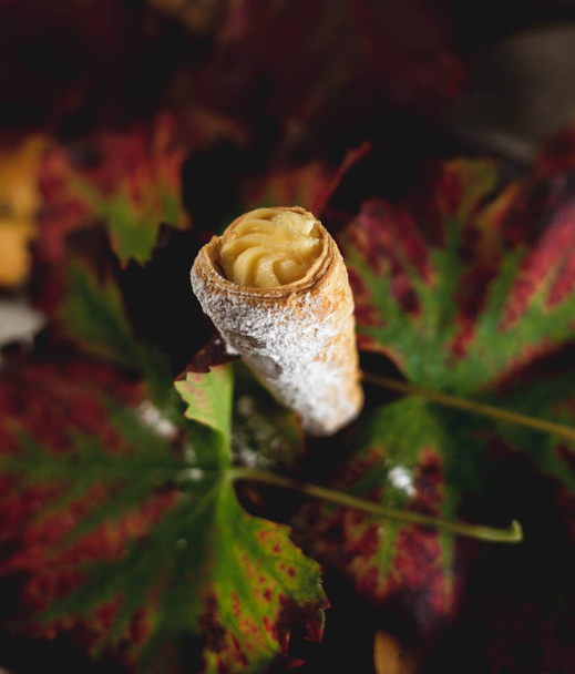 пирог в форме конуса, наполненный сливками, удерживаемыми осенними листьями - Фото, изображение