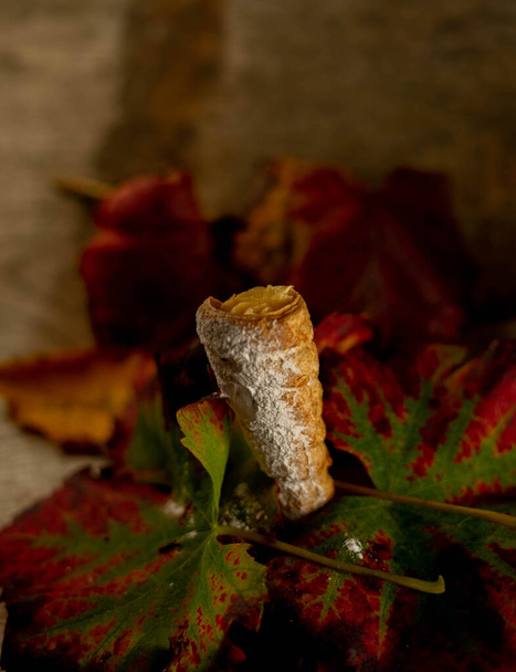 пирог в форме конуса, наполненный сливками, удерживаемыми осенними листьями - Фото, изображение