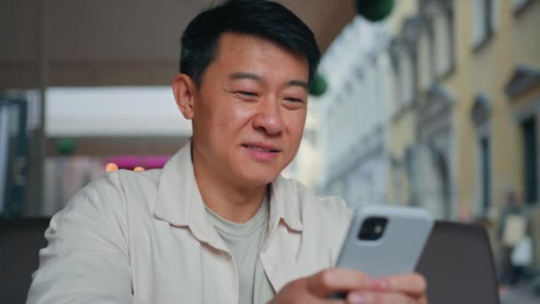 Yakın plan mutlu Asyalı adam cep telefonuyla sosyal ağda geziniyor akıllı telefon kullanarak erkek turist rezervasyon bileti alıyor internet sohbetlerinde e-posta iletileri gönderiyor çevrimiçi mağazada alışveriş yapıyor. - Video, Çekim