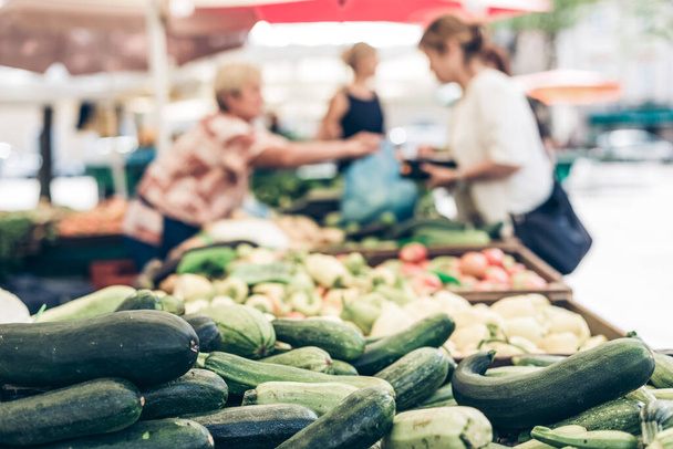 Bauernmarkt mit einer Vielfalt an Bio-Gemüse. Verkäufer bedient und plaudert mit Kunden. - Foto, Bild
