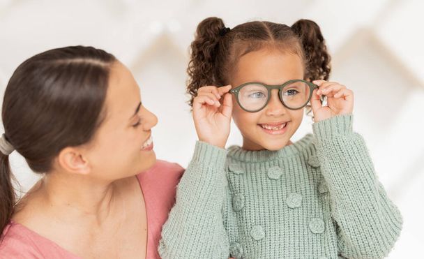 Οπτομετρία, όραση και μητέρα με παιδί με γυαλιά μετά από εξέταση, εξέταση και διάγνωση για όραση. Οικογένεια, υγειονομική περίθαλψη και χαρούμενο κορίτσι με νέα γυαλιά στο γραφείο του γιατρού μετά από οπτική εξέταση. - Φωτογραφία, εικόνα
