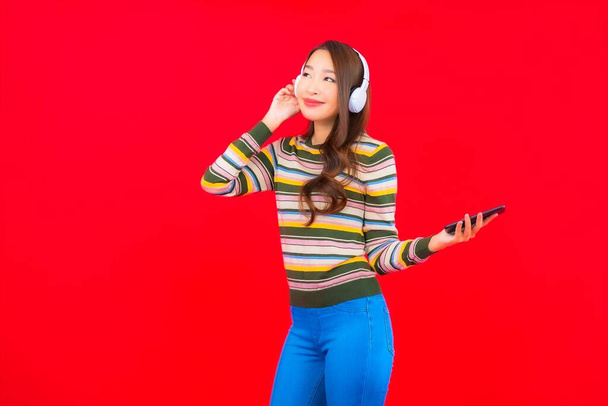 Πορτρέτο όμορφη νεαρή Ασιάτισσα γυναίκα χρησιμοποιούν έξυπνο κινητό τηλέφωνο με ακουστικά για να ακούσετε μουσική - Φωτογραφία, εικόνα