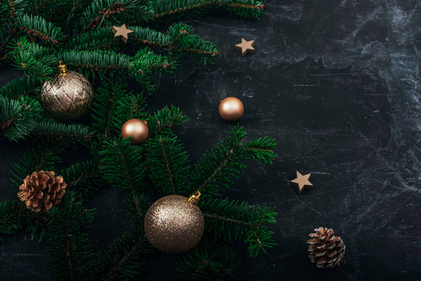 Christmas tree branches, golden baubles and pine cones on black background. New Year concept. Top view, copy space. - Foto, Bild