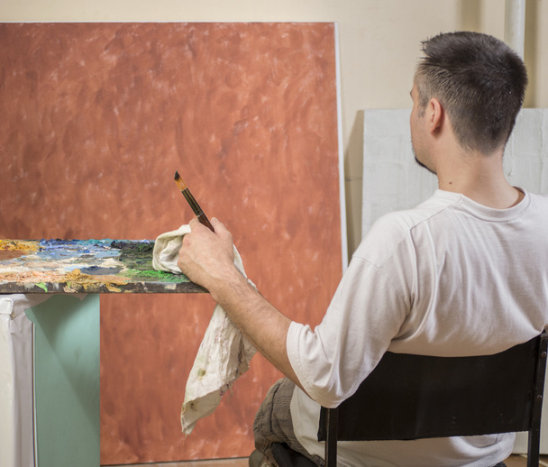 Painters back while sitting and analyzing his work - 写真・画像