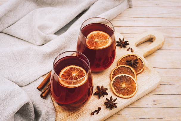 Two glasses with mulled wine on wooden cutting board with spices and orange slices, top view. - Photo, Image