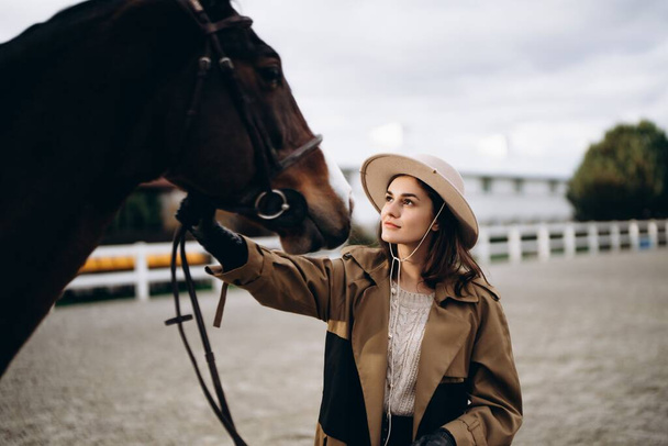 A young woman in a brown coat and hat near a horse. High quality photo - Foto, Bild
