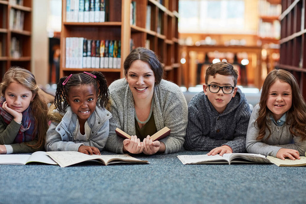 Γλυπτική νεαρά μυαλά με την ανάγνωση. μαθητές δημοτικού διαβάζοντας με το δάσκαλό τους στο πάτωμα της βιβλιοθήκης - Φωτογραφία, εικόνα
