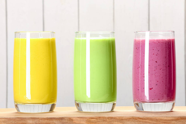 Board with many different tasty smoothies against white wooden background, closeup - Photo, image