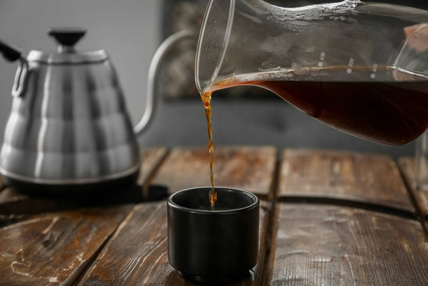 Kávé öntése csészébe a fa asztalnál a kávézóban - Fotó, kép