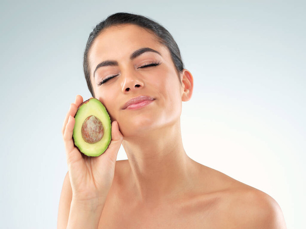 Youre all Ive avo wanted for a lovely skincare treatment. Studio portrait of a beautiful young woman covering her eye with an avocado against a gray background - Fotoğraf, Görsel