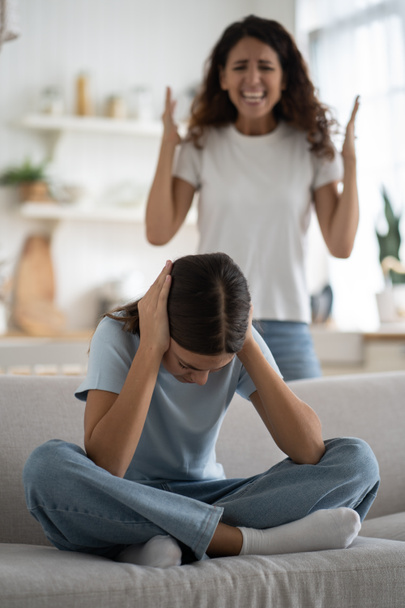 Naughty girl closing ears looks down sits on couch refusing to fulfill mother requests. Aggressive woman yells at daughter because of problems associated with transitional age in adolescent. Parenting - Photo, Image
