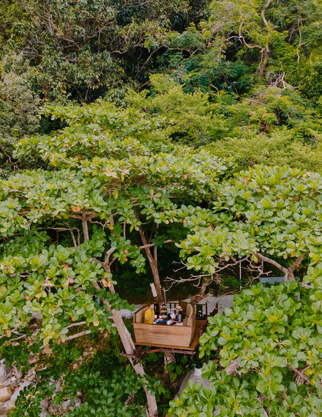 Vista del dron en el té de la tarde en una vaina de árbol en los árboles de la isla tropical Phuket Tailandia, un par de hombres y mujeres tomando té de la tarde en una cesta de red de aves - Foto, imagen