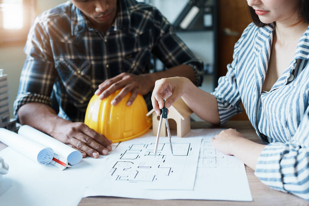 Engineers are consulting the team to design an architectural structure for clients with blueprints and building models to work at office. - 写真・画像