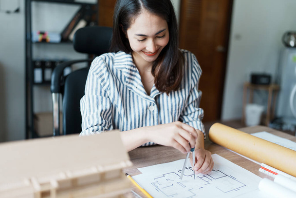 Portrait of an Asian female engineers are designing house structures and architectural using blueprints, rulers, pencils, dividers and building models to work. - 写真・画像