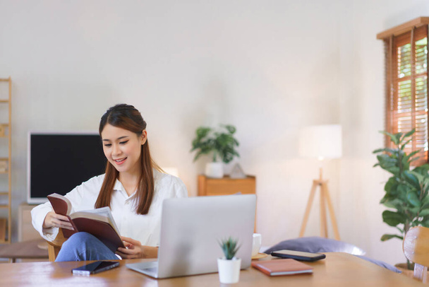 リラックスした時間の概念,現代の自宅のオフィスでラップトップで作業した後、女性は聖書を読んで. - 写真・画像