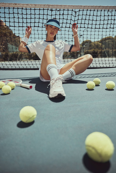 Relax, portrait and tennis woman at net on exercise, fitness and court break at sports ground. Training, workout and cardio of professional athlete club girl resting on floor with tennis balls - Photo, Image