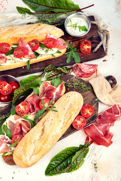 Two baguette sandwiches with salami, mozzarella cheese, lettuce, tomatoes and ham on a cutting boards. Long subway sandwiches on a white background. Top view. - Foto, immagini