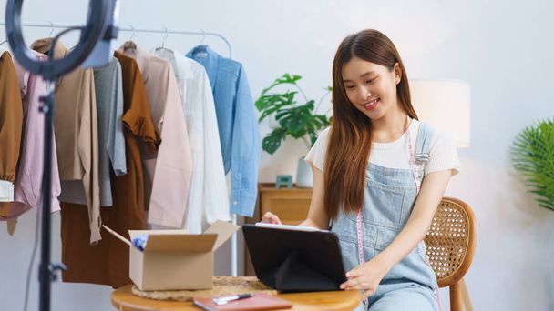オンラインショッピングのコンセプトは、アジアの女性はライブストリーム販売服の後にタブレット上の販売量をチェック. - 写真・画像