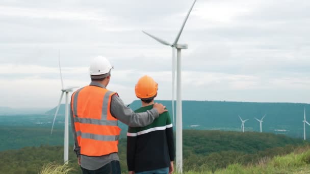 Ingenieur mit seinem Sohn auf einem Windpark auf einem Hügel oder Berg im ländlichen Raum. Progressives Ideal für die zukünftige Produktion erneuerbarer, nachhaltiger Energie. Energieerzeugung aus Windenergieanlagen. - Filmmaterial, Video