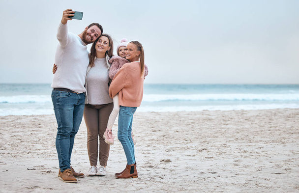 Strand, selfie en vrolijke familie glimlach, ontspannen en binden aan de oceaan, knuffelen en genieten van een reis in de natuur samen. Reizen, telefoon en familiefoto aan zee tijdens een vakantie in Canada met meisje en ouders. - Foto, afbeelding