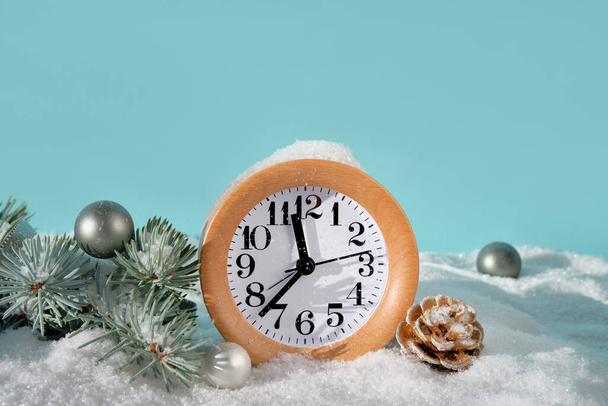 Wood alarm clock with fir twigs, green trinkets and snow. Time twenty to midnight. Off white and mint green background. Merry Christmas and Happy New Year. Copy-space, place for text. - Valokuva, kuva