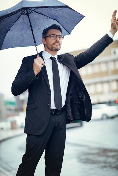 Hes a businessman on a mission. a mature businessman holding an umbrella and gesturing to get a cab in the city - Foto, immagini