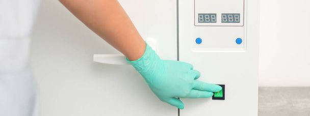 Schoonheidsspecialiste in beschermende handschoenen start de machine voor desinfectie van gereedschap voor de medische procedure - Foto, afbeelding