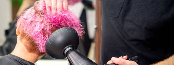 Séchage court rose coiffure bob d'une jeune femme caucasienne avec un sèche-cheveux noir avec la brosse par les mains d'un coiffeur masculin dans un salon de coiffure, gros plan - Photo, image