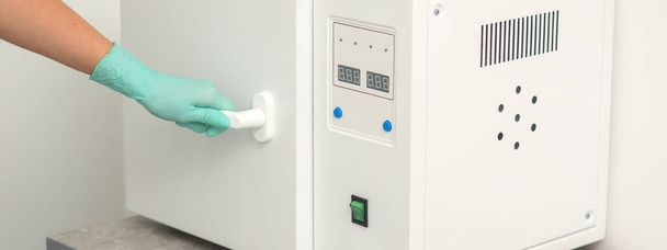 esteticista en guantes de protección cerrar la puerta de la máquina para la desinfección de herramientas antes de los procedimientos médicos - Foto, Imagen
