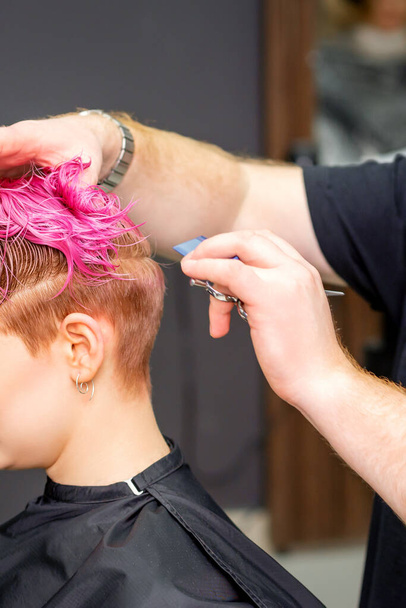 Fiatal kaukázusi nő festett rövid, rózsaszín, nedves hajának hajvágása egy férfi fodrász által egy fodrászatban - Fotó, kép